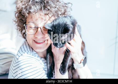 Lächelnde Frau mittleren Alters mit schwarzer Katze zu Hause Nahporträt Stockfoto