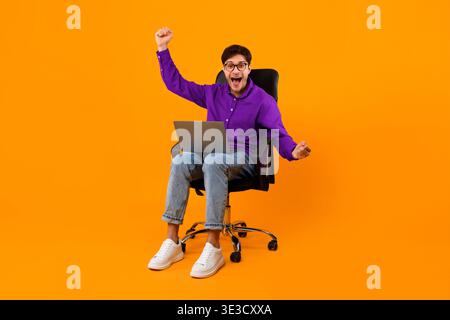 Aufgeregt junger Mann feiert Erfolg bei der Arbeit am Laptop in Bright Studio Stockfoto