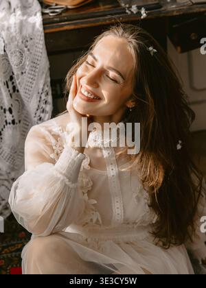 Traumhaftes, sonnendurchflutetes Porträt einer jungen Frau in Spitzenkleid, sanftem Lächeln und romantischer Vintage-Stimmung. Stockfoto