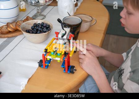 Boy montiert Bauspielzeug am Tisch mit Frühstücksartikeln im Innenraum mit natürlichem Licht, konzentrierter Aktivität und alltäglichem Lernmoment Stockfoto