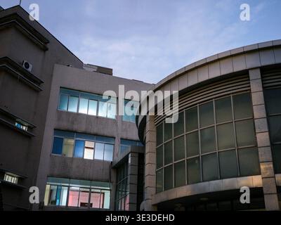 Eine moderne geschwungene Gebäudefassade mit horizontalen Betonbändern und großen Glasfenstern, die das sanfte Licht des Abendhimmels reflektieren. Der Szenenrep Stockfoto