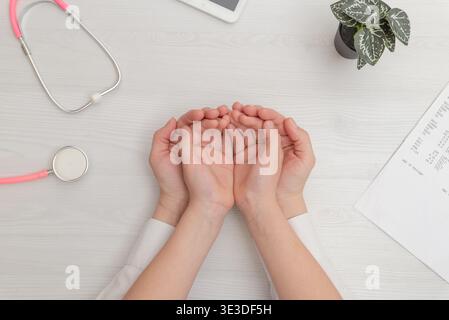 Arzt, der die Hände des Patienten in liebevoller Geste auf dem medizinischen Schreibtisch hält, steht für Vertrauen, Unterstützung und Gesundheitsschutzkonzept Stockfoto