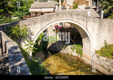 Mostar, Bosnien und Herzegowina - 05 27 2025: Angewinkeltes Kanonfoto von Kriva Ćuprija, das sich über den Radobolja-Fluss erhebt und von historischen Steinhäusern umgeben ist Stockfoto