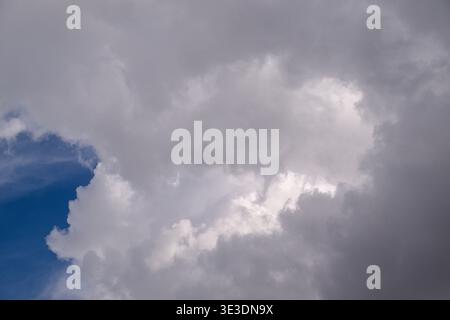 Wolken ziehen über den blauen Himmel, einige hellweiß, andere dunkelgrau. Sonnenlicht bricht durch Spalten in stürmischen Wolken. Der Himmel zeigt einen Kontrast zwischen ruhigem Blau Stockfoto