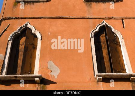 Typische antike venezianische Fenster mit gotischen Bögen und dunklen Holzläden und Steinfensterbänken in einer orangen Wand. Venedig, Italien Stockfoto