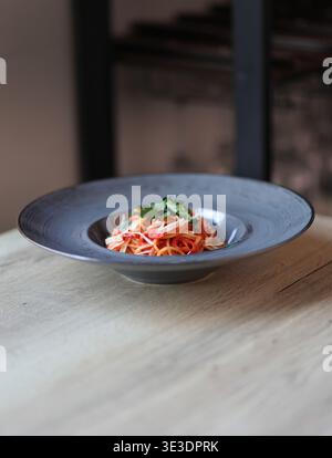 Spaghetti Arrabbiata mit würziger Tomatensauce, serviert auf einem blauen Teller in einem feinen Speisestil mit sanfter Beleuchtung. Stockfoto