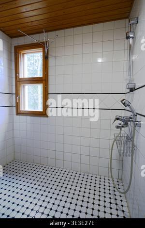 Sauberes und einfaches Badezimmer mit gefliestem Duschbereich, Holzdecken- und Fensterrahmen, Handbrause und natürlichem Licht Stockfoto