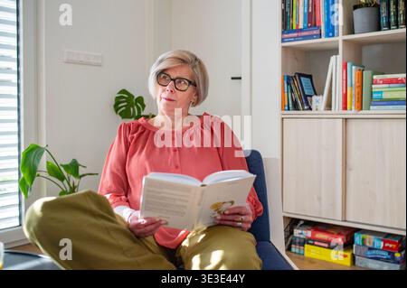 Lächelnde ältere Frau, die zu Hause Buch liest. Stockfoto