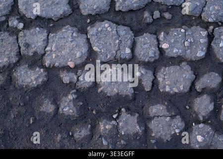 Beschädigte Asphaltoberfläche mit gerissenen Stellen und freiliegenden Kiessteinen. Detaillierter Hintergrund mit verwitterter Textur einer kaputten Straße oder eines Gehwegs für urb Stockfoto