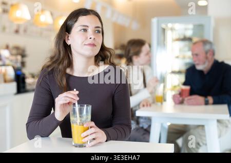 Frau, die am Tisch sitzt und frisch Orangensaft trinkt Stockfoto