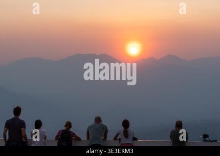 Wat Phra That Mae Yen, Pai, Thailand – 11. März 2020: Besucher beobachten den Sonnenuntergang über trüben Bergsilhouetten von einem Aussichtspunkt auf einem Hügel. Stockfoto
