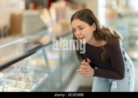 Die junge Frau wählt mit Interesse aus, welchen Geschmack Eis sie probieren soll Stockfoto