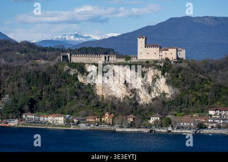 Tele-Blick auf die mittelalterliche Festung Rocca di Angera über dem Lago Maggiore mit schneebedeckten Alpen unter klarem blauem Himmel. Stockfoto