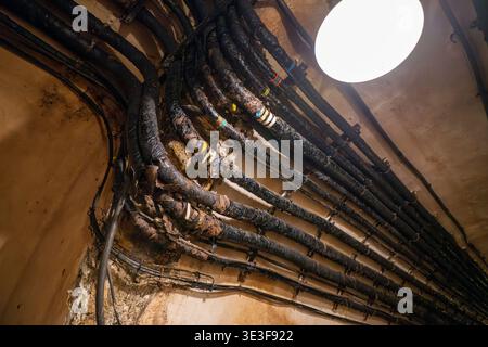 Nahaufnahme von gebündelten isolierten Kabeln und Kabeln unter einer runden Deckenleuchte in einem abgenutzten unterirdischen Durchgang bei Ouvrage Hackenberg, Maginot Line Festung Stockfoto