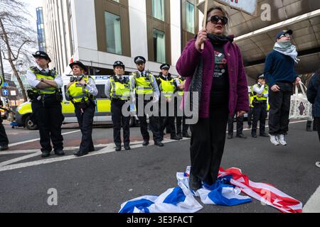 Ein Demonstrant steht auf der Flagge der USA und Israels, während die Polizei während der Kundgebung zusieht. Demonstranten versammelten sich vor der Botschaft der Vereinigten Staaten in neun Elms zu einer Demonstration gegen US-amerikanische und israelische Militäraktionen im Nahen Osten, einschließlich des anhaltenden Krieges mit dem Iran und des anhaltenden Konflikts in Gaza. Der von pro-palästinensischen und Antikriegsgruppen organisierte marsch bewegte sich Richtung Victoria, wo die Teilnehmer auf der Straße gingen und von der Polizei auf der Strecke herausgefordert wurden. Demonstranten trugen Fahnen und Plakate und skandierten Slogans gegen die westliche Intervention und drückten ihre Solidarität mit coun aus Stockfoto