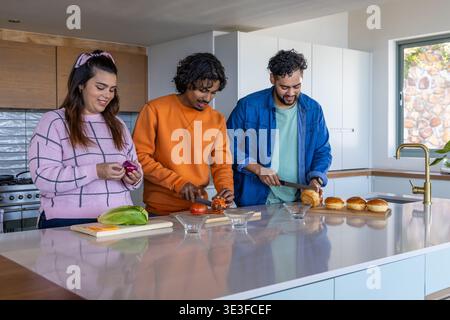 Verschiedene Freunde bereiten Burger-Zutaten auf der Hochglanzinsel zu Hause mit Kochmessern vor Stockfoto