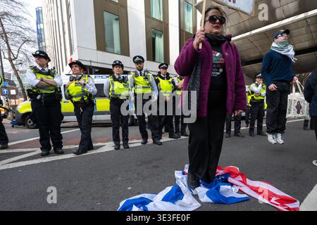 Ein Demonstrant steht auf der Flagge der USA und Israels, während die Polizei während der Kundgebung zusieht. Demonstranten versammelten sich vor der Botschaft der Vereinigten Staaten in neun Elms zu einer Demonstration gegen US-amerikanische und israelische Militäraktionen im Nahen Osten, einschließlich des anhaltenden Krieges mit dem Iran und des anhaltenden Konflikts in Gaza. Der von pro-palästinensischen und Antikriegsgruppen organisierte marsch bewegte sich Richtung Victoria, wo die Teilnehmer auf der Straße gingen und von der Polizei auf der Strecke herausgefordert wurden. Demonstranten trugen Fahnen und Plakate und skandierten Slogans gegen die westliche Intervention und drückten ihre Solidarität mit coun aus Stockfoto