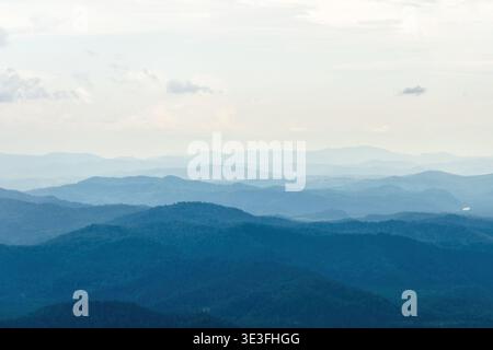 Weitläufige blaue Bergkette mit atmosphärischen Nebelschichten, die in einen weichen Himmel fallen. Beschwört Ruhe, Natur und friedliche Flucht Stockfoto
