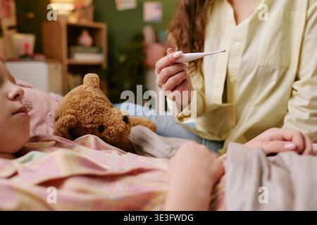 Kind liegt im Bett, während Erwachsene Frau Temperatur überprüft Stockfoto