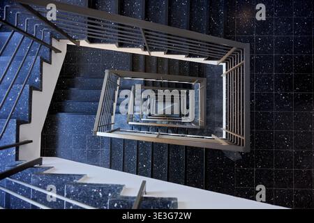 Eine fesselnde Aufnahme einer modernen Wendeltreppe, die geometrische Präzision und sich wiederholende Muster zeigt. Dunkles, gesprenkeltes Terrazzo tritt an Stockfoto