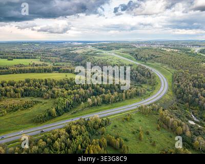 Drohnenfoto, das die verwinkelte Autobahninfrastruktur durch landwirtschaftliche Felder und Mischwälder zeigt, wie sich die Verkehrsentwicklung in der Landschaft von Kuzbass entwickelt, selektiver Fokus Stockfoto
