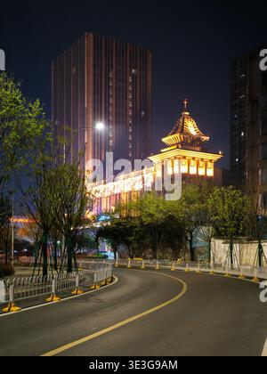 Wuhan, China - 23. März 2025: Eine kurvige Stadtstraße in der Nacht, die zu einem hell beleuchteten Gebäude im traditionellen Stil und einem modernen Wolkenkratzer führt. Das ima Stockfoto