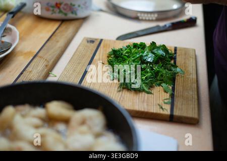 Das Essen wird auf dem Herd gekocht, gehackte Petersilie, Dill und andere Grünsorten auf einem Stapel stehen auf dem Tisch. Authentisches Fotokochen DMA. Hochwertige Fotos Stockfoto