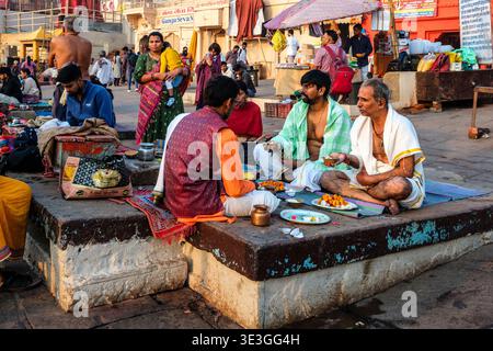 Die Menschen versammeln sich auf einer Steinplattform in Dashwamedh Ghat in Varanasi, um traditionelle Rituale mit einem Priester am Fluss Ganges durchzuführen. Stockfoto