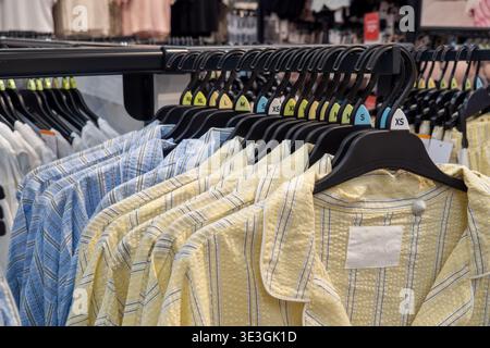Reihen farbenfroher Pyjamohemden hängen ordentlich an schwarzen Kleiderbügeln. Stockfoto
