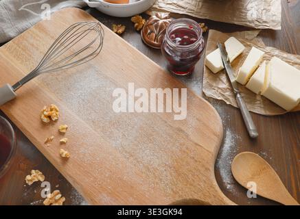 Schneidebrett aus Holz mit Mehl-Kopierraum und Backzutaten. Hochwinkelaufnahme des rustikalen Küchentisches mit bemehltem Holzbrett und Schneebesen Stockfoto