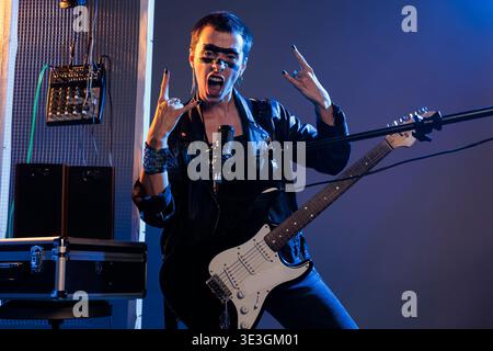 Punk Rocker, der Rock-Zeichen auf der Live-Vorstellung macht, und laute alternative Heavy-Metal-Musik singt. Mit Mikrofon und Gitarre cooles Solo-Lied spielen, Lederjacke tragen und Rock auf Symbol zeigen. Stockfoto