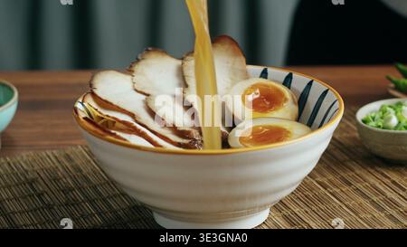 Der Koch gießt heiße herzhafte Brühe in eine Schüssel authentischer japanischer Ramen Stockfoto