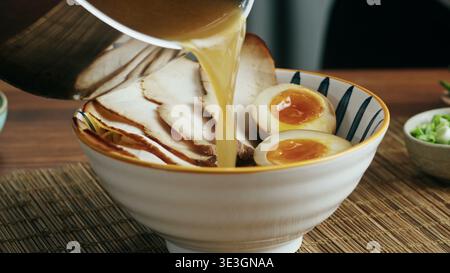 Der Koch gießt heiße herzhafte Brühe in eine Schüssel authentischer japanischer Ramen Stockfoto