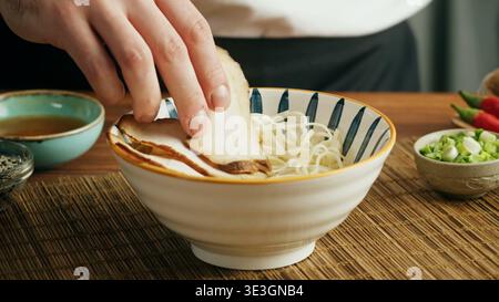 Ein professioneller Koch fügt eine Schüssel mit traditionellen Ramen Schweinebraten hinzu Stockfoto