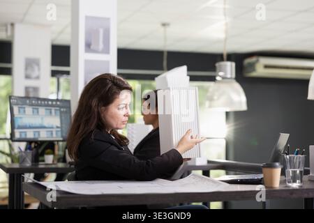 Kaukasierin nutzt Laptop für virtuelle Meetings, um Architekturlayouts mit Remote-Kunden zu besprechen. Professionelle Architektin, die Bauunternehmern während eines Videogesprächs ein Miniaturmodell zeigt Stockfoto