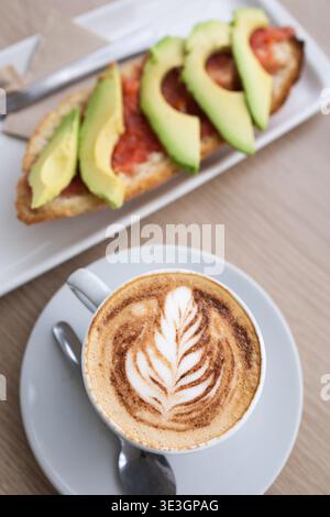 Köstliches Frühstück mit einem Cappuccino mit Latte Art und einem Toast mit frischen Tomaten und Avocado Stockfoto