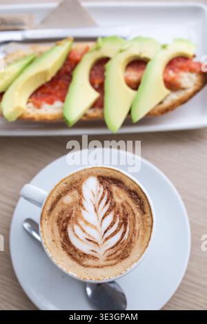 Köstliches Frühstück mit einem Cappuccino mit Latte Art und einem Toast mit frischen Tomaten und Avocado Stockfoto