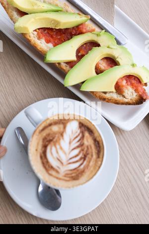 Köstliches Frühstück mit einem Cappuccino mit Latte Art und einem Toast mit frischen Tomaten und Avocado Stockfoto