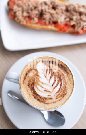 Köstliches Frühstück mit einem Cappuccino mit Latte Art und einem Toast mit Tomaten und Thunfisch Stockfoto