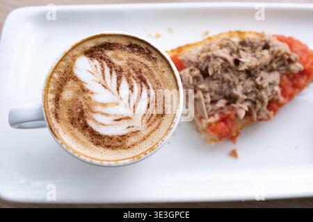 Köstliches Frühstück mit einem Cappuccino mit Latte Art und einem Toast mit Tomaten und Thunfisch Stockfoto