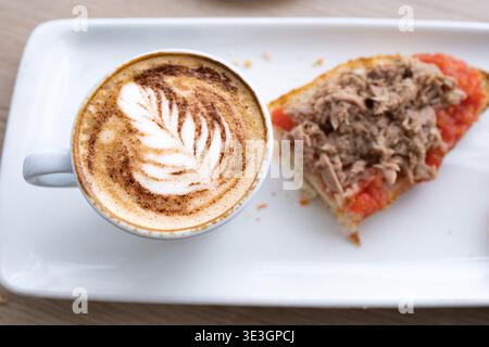 Köstliches Frühstück mit einem Cappuccino mit Latte Art und einem Toast mit Tomaten und Thunfisch Stockfoto