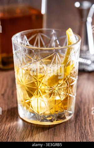 Rostiger Nagelcocktail mit Zitronenschale in Kristallglas auf Holztisch Stockfoto