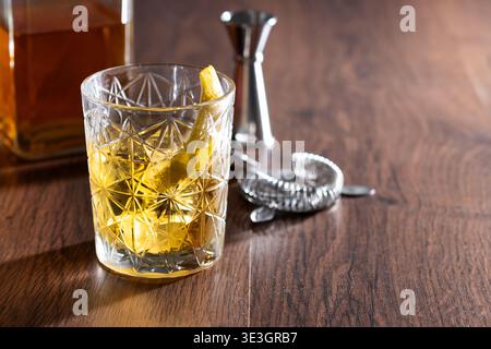 Rostiger Nagelcocktail mit Zitronenschale in Kristallglas auf Holztisch Stockfoto