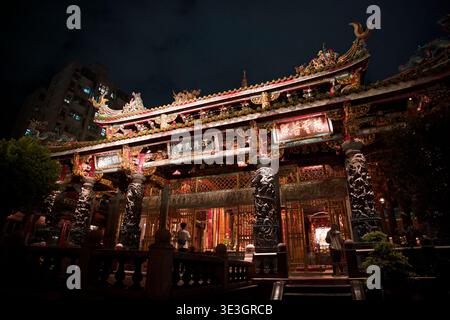 Taipeh, Taiwan - 10. August 2023: Bangka Longshan Tempel leuchtet nachts mit verzierten goldenen Fassaden, Drachensäulen und traditionellem taiwanesischen Tempel. Stockfoto