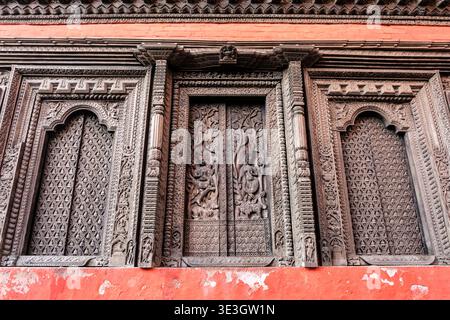 Die rote Außenwand von Shree Annapurna Mandir in Varanasi verfügt über dunkle, tief versenkte Holzfenster mit aufwendigen traditionellen Schnitzereien. Stockfoto