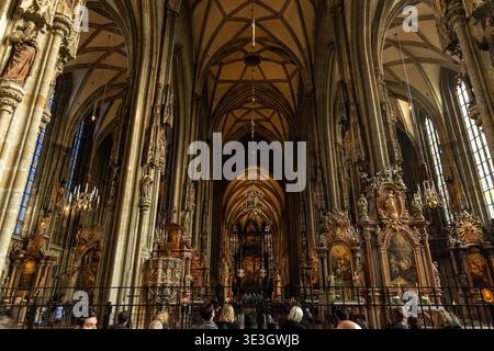 Der Blick auf die hoch aufragende gotische Architektur, detaillierte Schnitzereien und warmes Licht durch Buntglasfenster schaffen eine beeindruckende Atmosphäre. Stockfoto