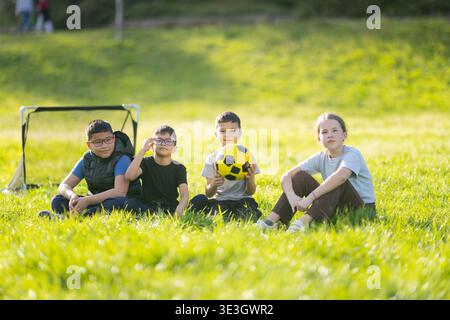 Verschiedene Kindergruppen, die sich während des Fußballspiels auf dem Gras ausruhen Stockfoto