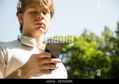 Junger kaukasischer Mann hört Musik und hält Handy in der Natur Sommer Hintergrund. Überprüfen Sie Apps, die sich auf das Gerät konzentrieren, chatten oder im Internet surfen. Im Freien. || Modell freigegeben Stockfoto