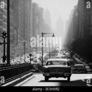 Dieses alte Straßenfoto von Angelo Rizzuto, wahrscheinlich aus den 1950er Jahren, zeigt einen Blick auf eine belebte Park Avenue in New York City. Die Szene zeigt die Rückseite eines Autos mit offener Tür, einen geschlossenen Mittelstreifen und die hoch aufragenden Silhouetten von Hochhäusern, die in die Ferne fallen und eine klassische urbane Atmosphäre vermitteln. Stockfoto