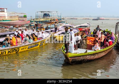 Passagiere in traditioneller Kleidung sitzen auf gelben Holzbooten am Ganges in Varanasi, während sie sich auf eine Fahrt über das Wasser vorbereiten. Stockfoto